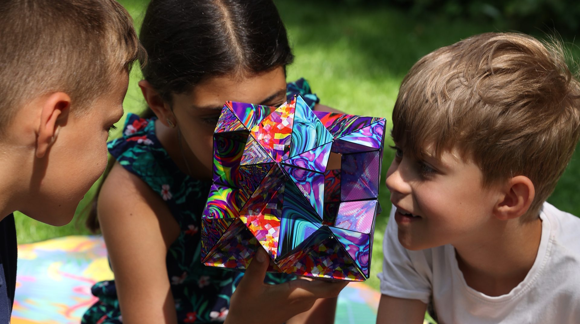 Two kids peering through an unfolded Shashibo magnetic puzzle